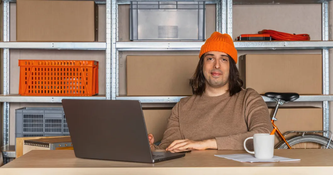 Man med orange mössa sitter bakom en bärbar dator och ler