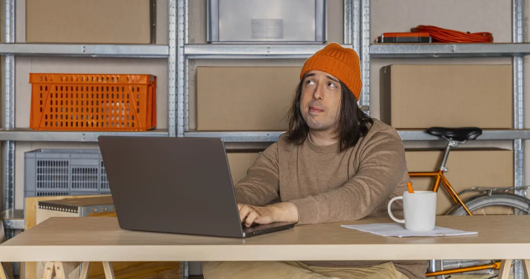 Man med orange mössa som jobbar med sin bärbara dator och tänker