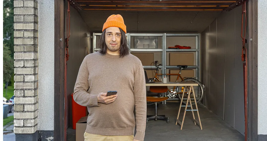 Man med orange hatt och smartphone i handen står framför ett garage